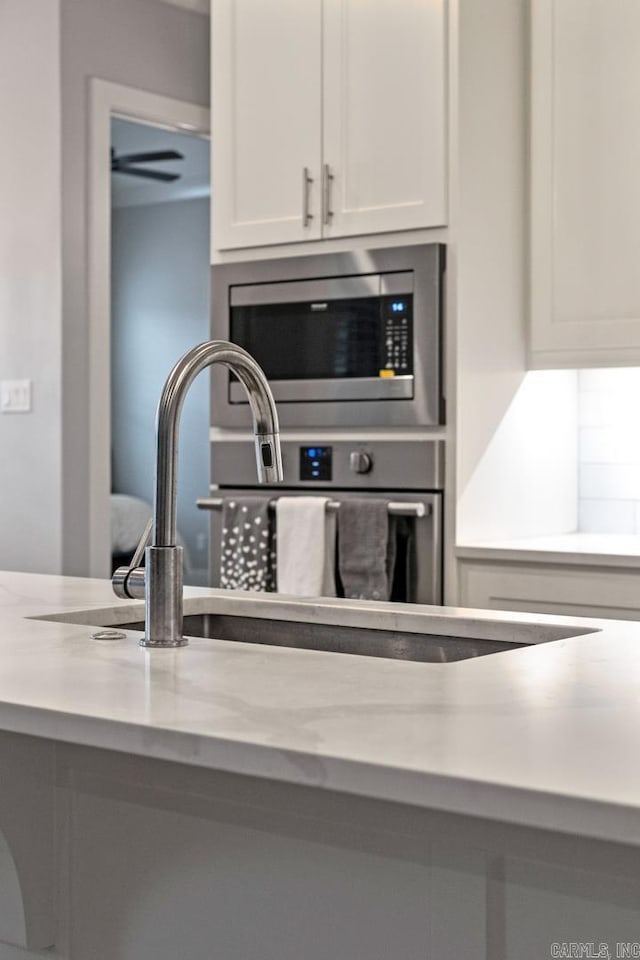 kitchen with light stone countertops, stainless steel microwave, and white cabinets