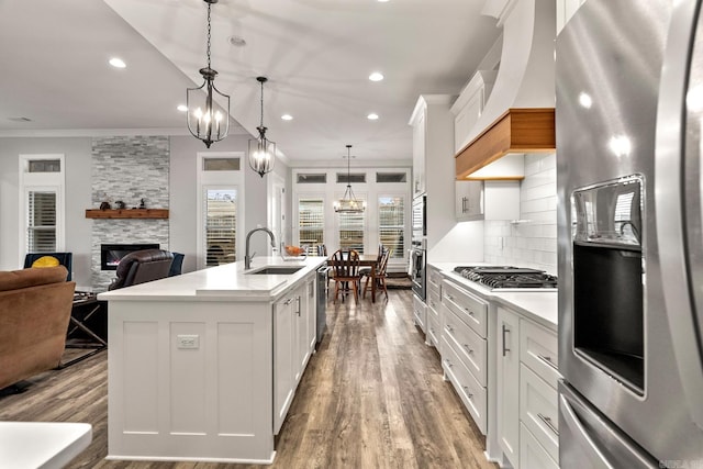 kitchen featuring a center island with sink, a stone fireplace, sink, white cabinetry, and stainless steel appliances