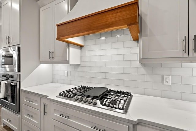 kitchen with premium range hood, tasteful backsplash, light stone counters, white cabinetry, and stainless steel appliances