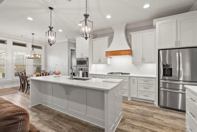 kitchen with white cabinets, hanging light fixtures, sink, appliances with stainless steel finishes, and custom range hood