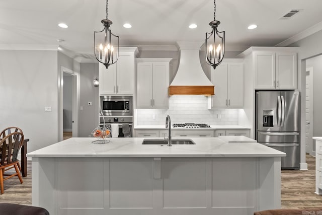 kitchen featuring appliances with stainless steel finishes, decorative light fixtures, a kitchen island with sink, and custom exhaust hood