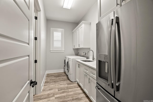 laundry room featuring separate washer and dryer, sink, cabinets, and light hardwood / wood-style floors