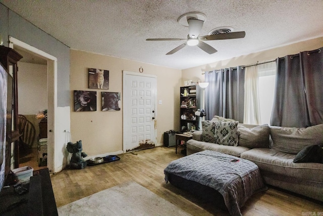 living room featuring ceiling fan, light wood-type flooring, and a textured ceiling