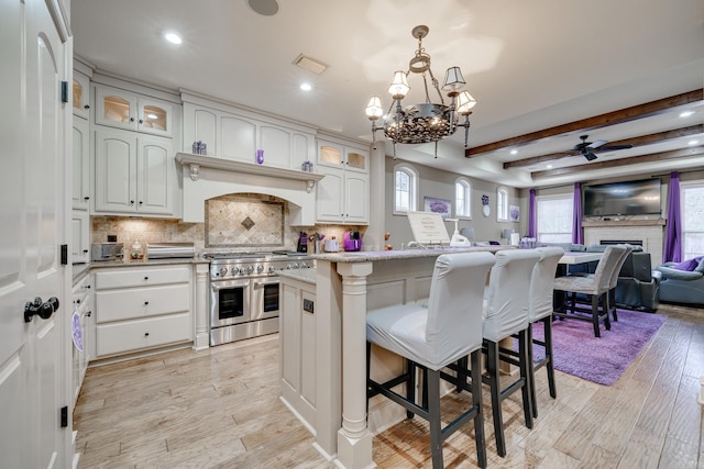 kitchen featuring double oven range, beamed ceiling, a center island, white cabinetry, and a breakfast bar area