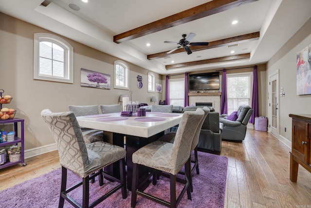 dining space featuring a raised ceiling, light hardwood / wood-style flooring, ceiling fan, and a stone fireplace