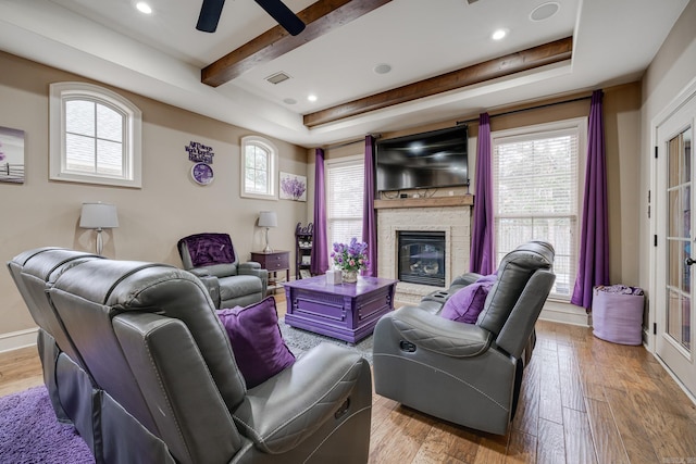 living room featuring a fireplace, light hardwood / wood-style flooring, a raised ceiling, and ceiling fan