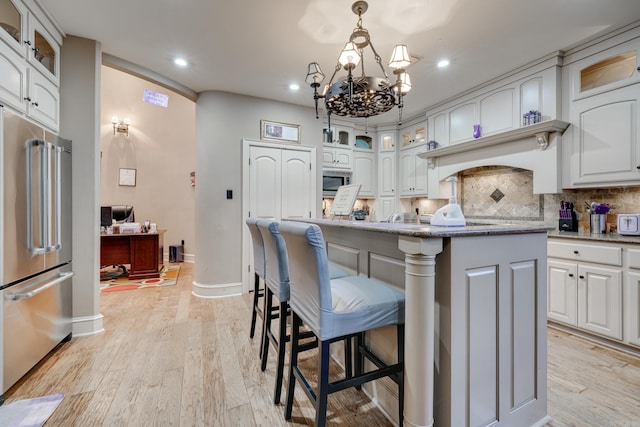 kitchen with white cabinetry, stainless steel appliances, light stone counters, pendant lighting, and a kitchen island