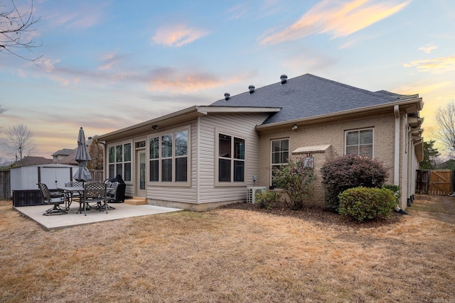 back house at dusk featuring a patio, a storage unit, and a lawn