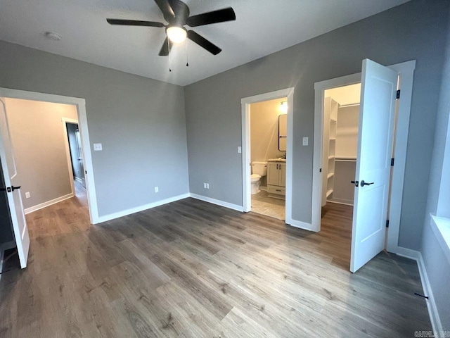 unfurnished bedroom with hardwood / wood-style floors, a walk in closet, ceiling fan, ensuite bath, and a closet