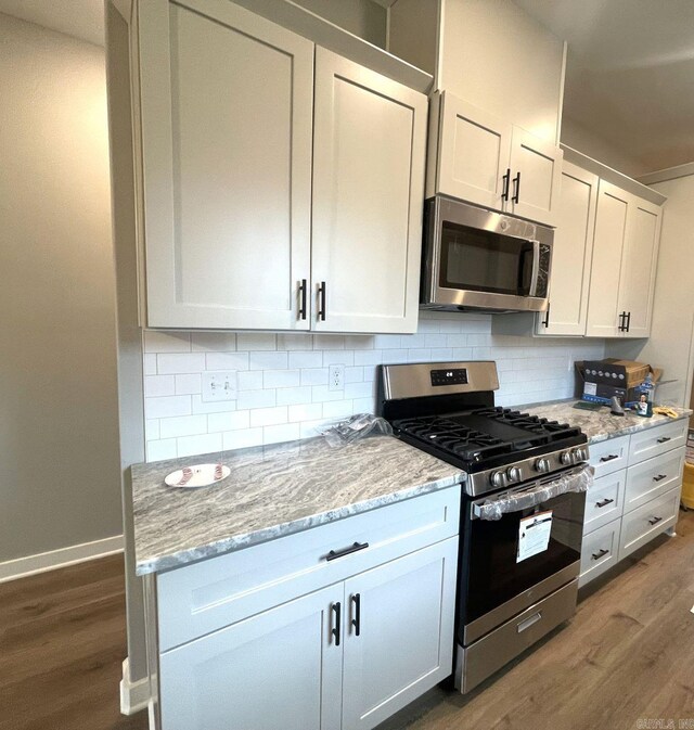 kitchen with light stone counters, tasteful backsplash, wood-type flooring, appliances with stainless steel finishes, and white cabinets