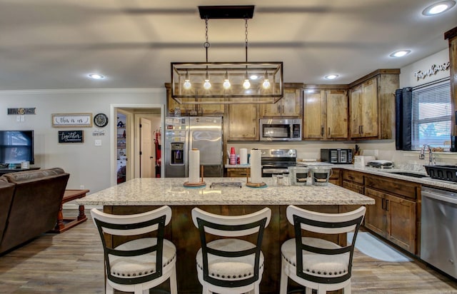 kitchen with sink, stainless steel appliances, decorative light fixtures, a breakfast bar, and a kitchen island