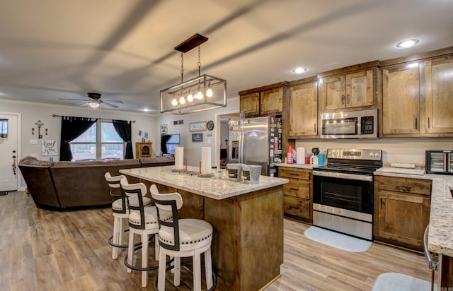 kitchen featuring a kitchen breakfast bar, hanging light fixtures, ceiling fan, a kitchen island, and stainless steel appliances