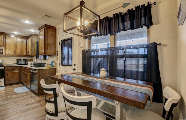 kitchen with appliances with stainless steel finishes, crown molding, sink, an inviting chandelier, and light hardwood / wood-style flooring