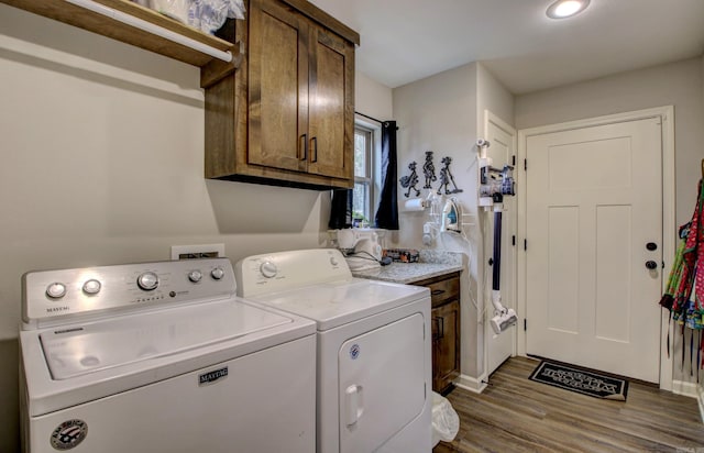 clothes washing area with washing machine and clothes dryer, hardwood / wood-style floors, and cabinets