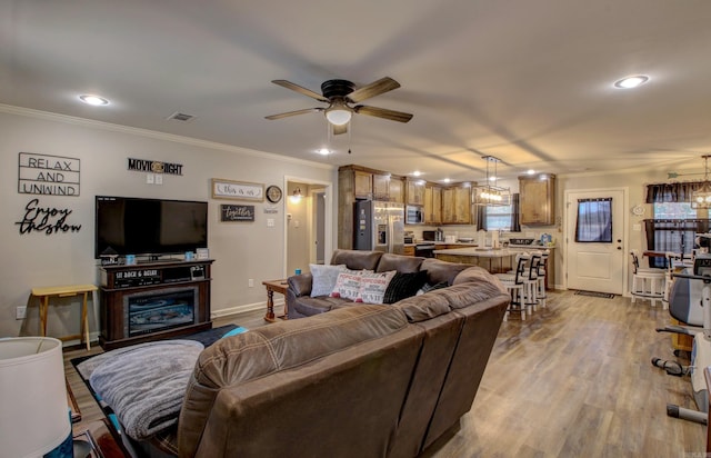 living room featuring ceiling fan, ornamental molding, and light wood-type flooring