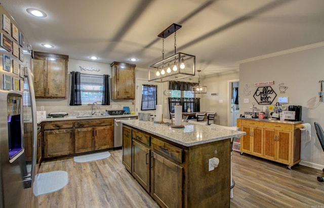 kitchen with ornamental molding, wood-type flooring, dishwasher, a kitchen island, and hanging light fixtures