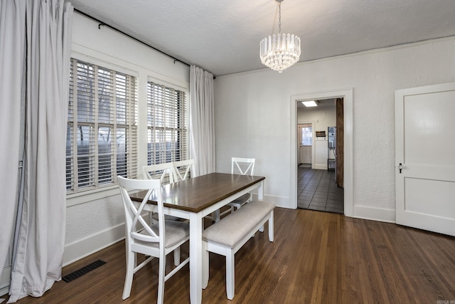 dining space with dark wood-type flooring, a textured ceiling, and an inviting chandelier