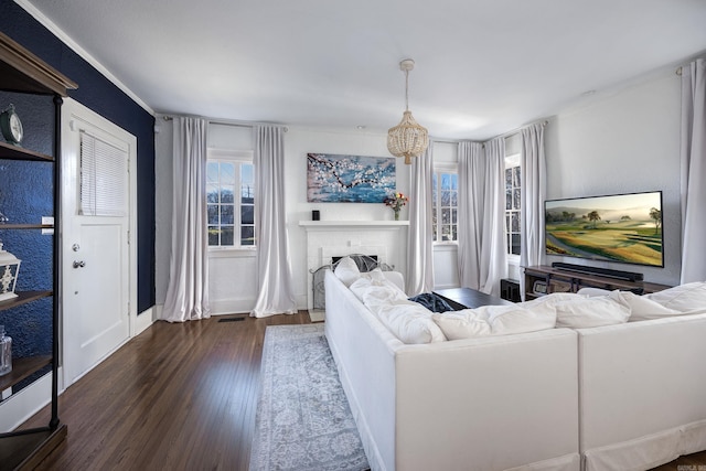 living room with an inviting chandelier, crown molding, dark wood-type flooring, and a brick fireplace