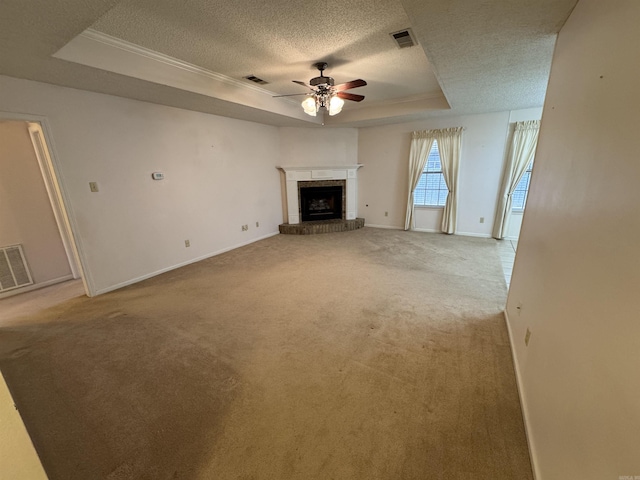 unfurnished living room with a brick fireplace, ceiling fan, carpet floors, and a tray ceiling