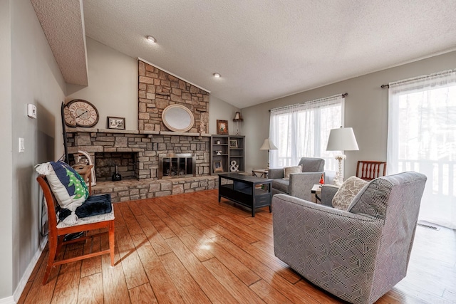 living room featuring lofted ceiling, a fireplace, a textured ceiling, and light hardwood / wood-style floors