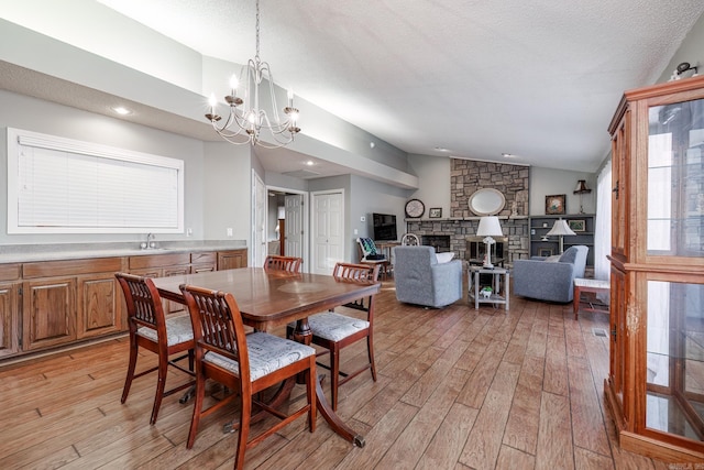 dining space with a stone fireplace, a chandelier, light wood-type flooring, sink, and lofted ceiling