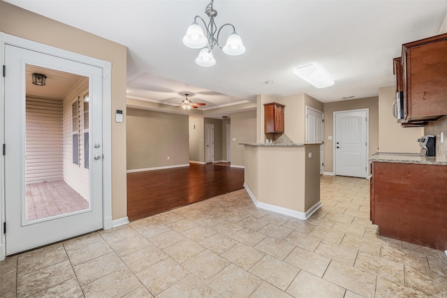 kitchen featuring pendant lighting, stove, ceiling fan with notable chandelier, decorative backsplash, and light stone countertops