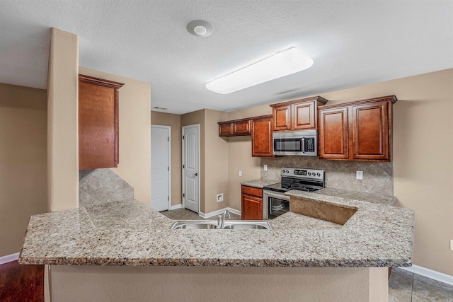 kitchen with kitchen peninsula, light stone countertops, backsplash, stainless steel appliances, and sink