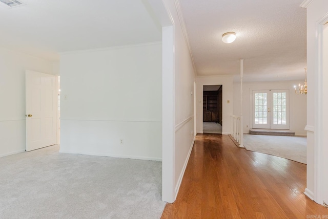 hall with carpet, french doors, ornamental molding, a textured ceiling, and a notable chandelier