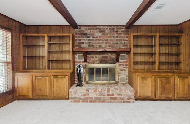 unfurnished living room featuring beamed ceiling, wood walls, light colored carpet, and a brick fireplace