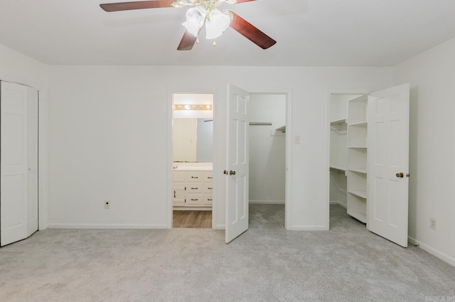 unfurnished bedroom featuring a walk in closet, ensuite bathroom, ceiling fan, and light colored carpet