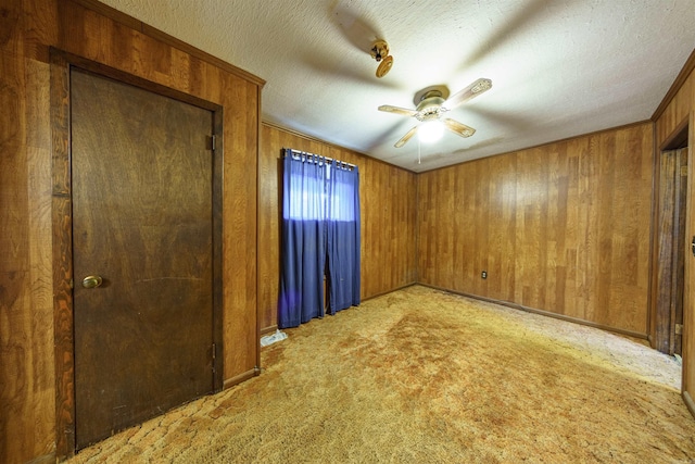 carpeted empty room featuring a textured ceiling, ceiling fan, and wooden walls