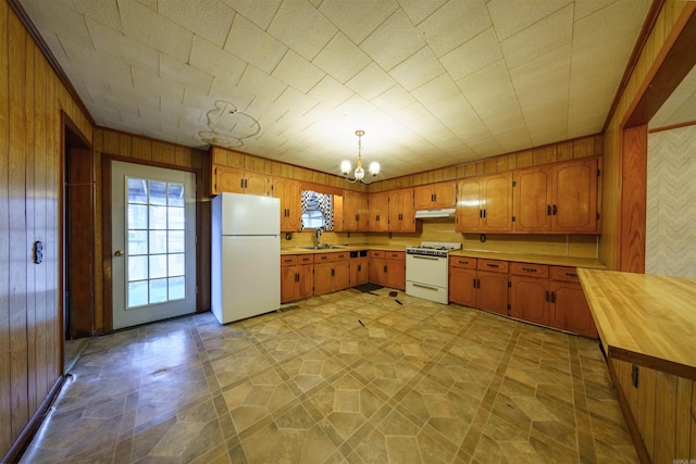 kitchen with white appliances, wooden walls, sink, decorative light fixtures, and a chandelier