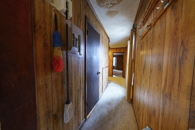 hall with a textured ceiling, light colored carpet, and wood walls