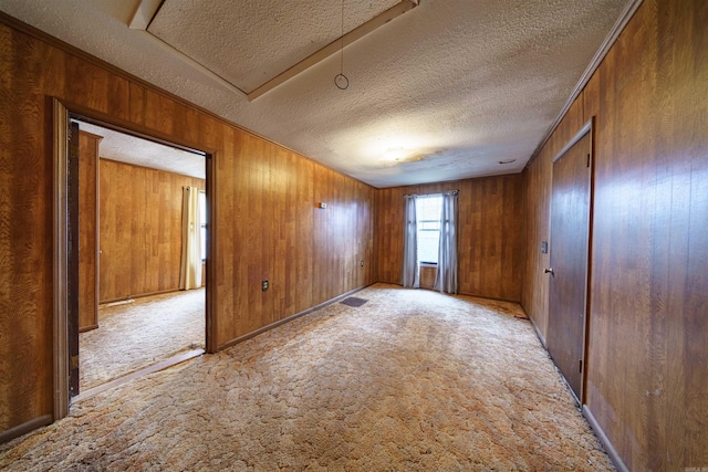 carpeted empty room with wooden walls and a textured ceiling