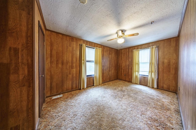 unfurnished room featuring a textured ceiling, ceiling fan, light carpet, and wooden walls