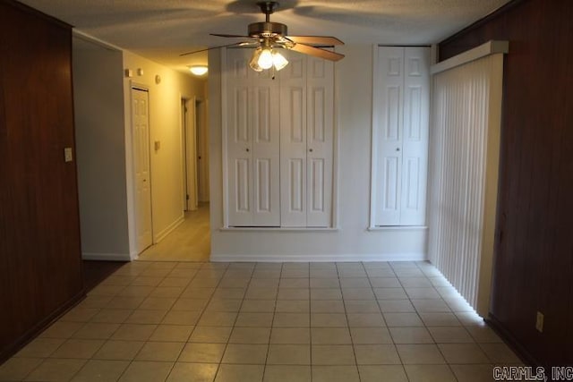 unfurnished room featuring ceiling fan, light tile patterned floors, a textured ceiling, and wooden walls