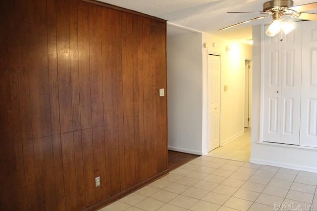 unfurnished room with light tile patterned floors, a textured ceiling, ceiling fan, and wooden walls