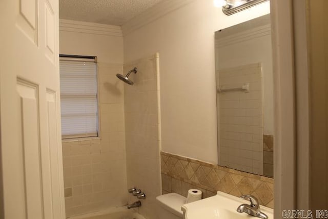 full bathroom with a textured ceiling, tiled shower / bath combo, sink, tile walls, and toilet