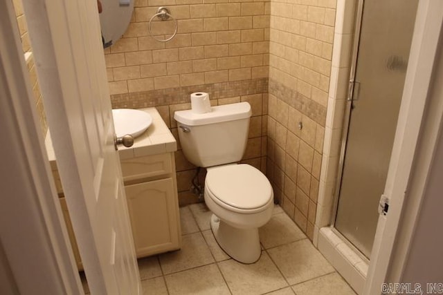 bathroom with tile patterned floors, toilet, a shower with door, vanity, and tile walls