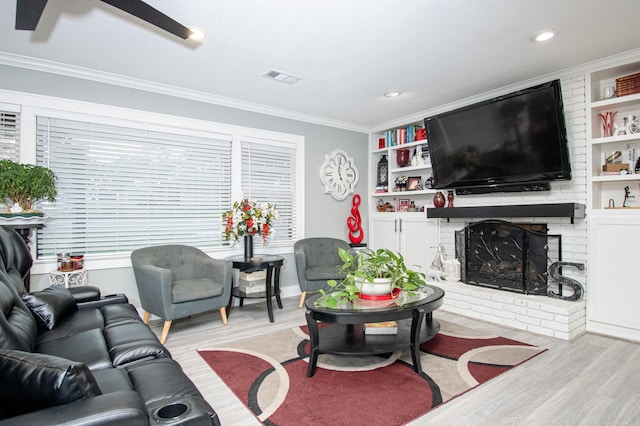 living room with built in shelves, a wealth of natural light, light wood-type flooring, a fireplace, and ornamental molding