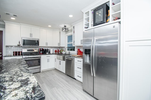 kitchen with decorative backsplash, dark stone counters, stainless steel appliances, light hardwood / wood-style flooring, and white cabinets