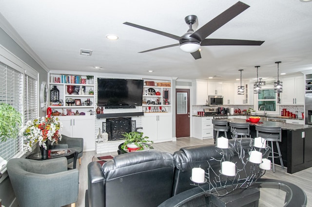 living room with ceiling fan, sink, light wood-type flooring, and crown molding