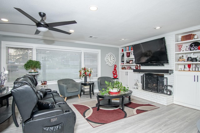 living room with ornamental molding, built in shelves, ceiling fan, light hardwood / wood-style flooring, and a fireplace