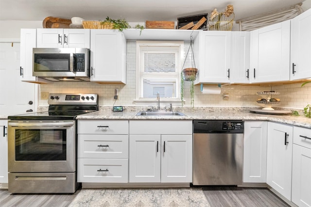 kitchen with white cabinetry, sink, stainless steel appliances, light hardwood / wood-style flooring, and backsplash