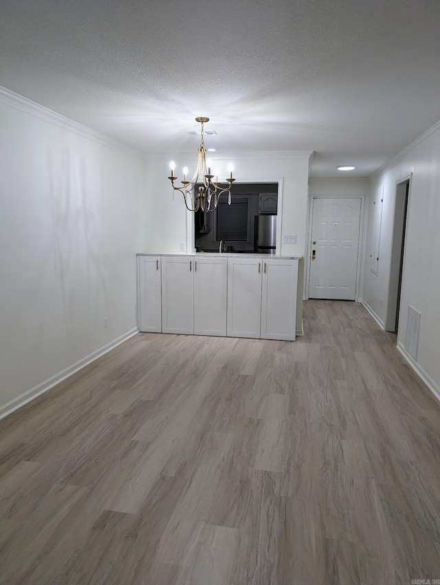 interior space featuring light wood-type flooring, ornamental molding, a textured ceiling, and a notable chandelier