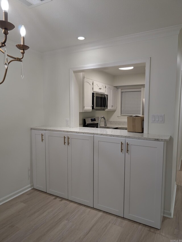 kitchen with white cabinets, ornamental molding, electric range oven, and a notable chandelier