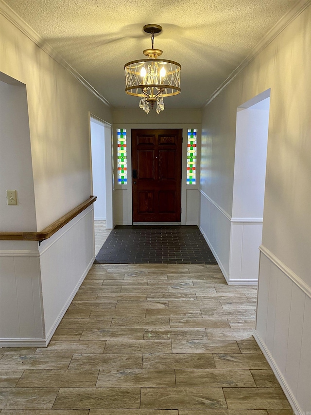 entryway featuring a textured ceiling, crown molding, and a chandelier