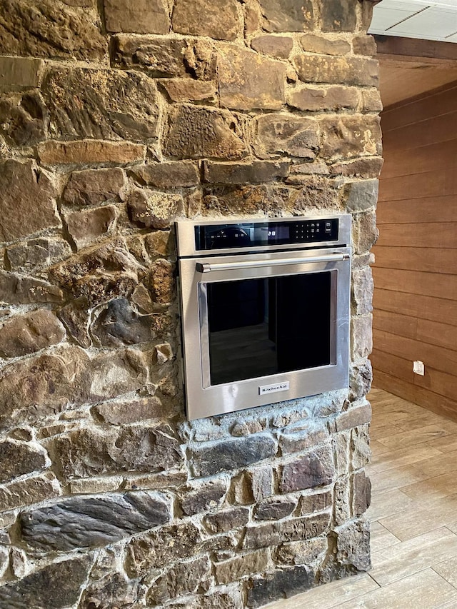 room details with light wood-type flooring, wooden walls, and stainless steel oven