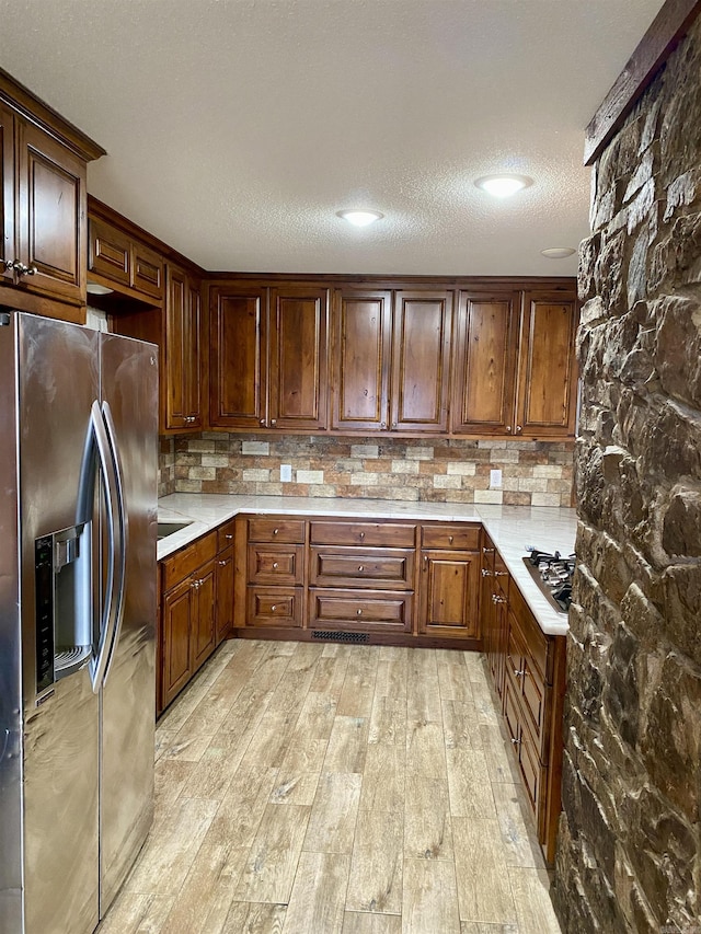 kitchen with a textured ceiling, stainless steel appliances, and light hardwood / wood-style flooring