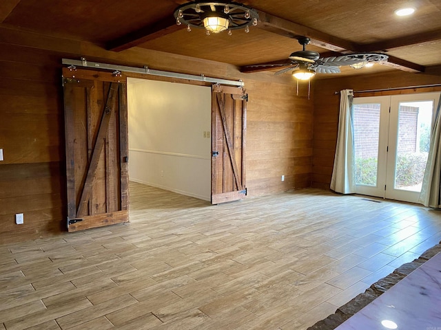 unfurnished room with ceiling fan, wooden walls, beam ceiling, a barn door, and wooden ceiling